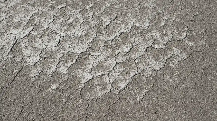 Aged foam roof surface with visible white coating thinning and gray discoloration patches spreading across south-facing slope, soft morning light revealing texture loss.