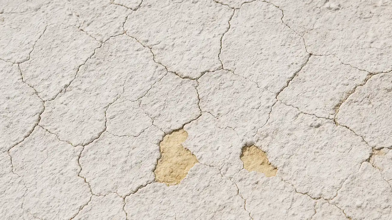 Close-up of aged spray foam roof surface showing white chalking, hairline cracks, and thin worn patches exposing yellow foam underneath in daylight.